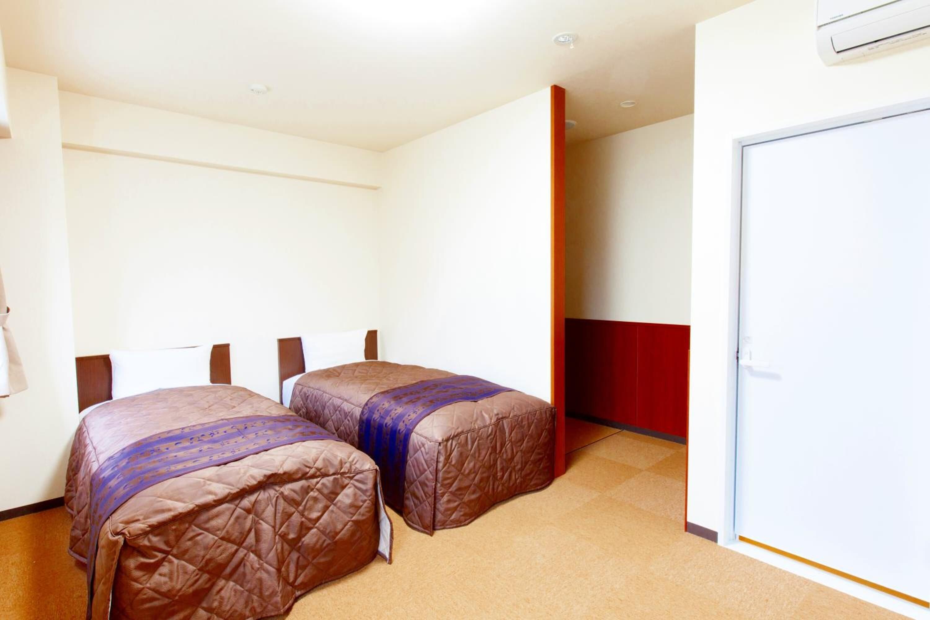 Une chambre d’hôtel avec deux lits, un mur d’accent rouge et une porte blanche.