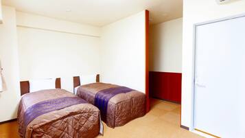 Une chambre d’hôtel avec deux lits, un mur d’accent rouge et une porte blanche.
