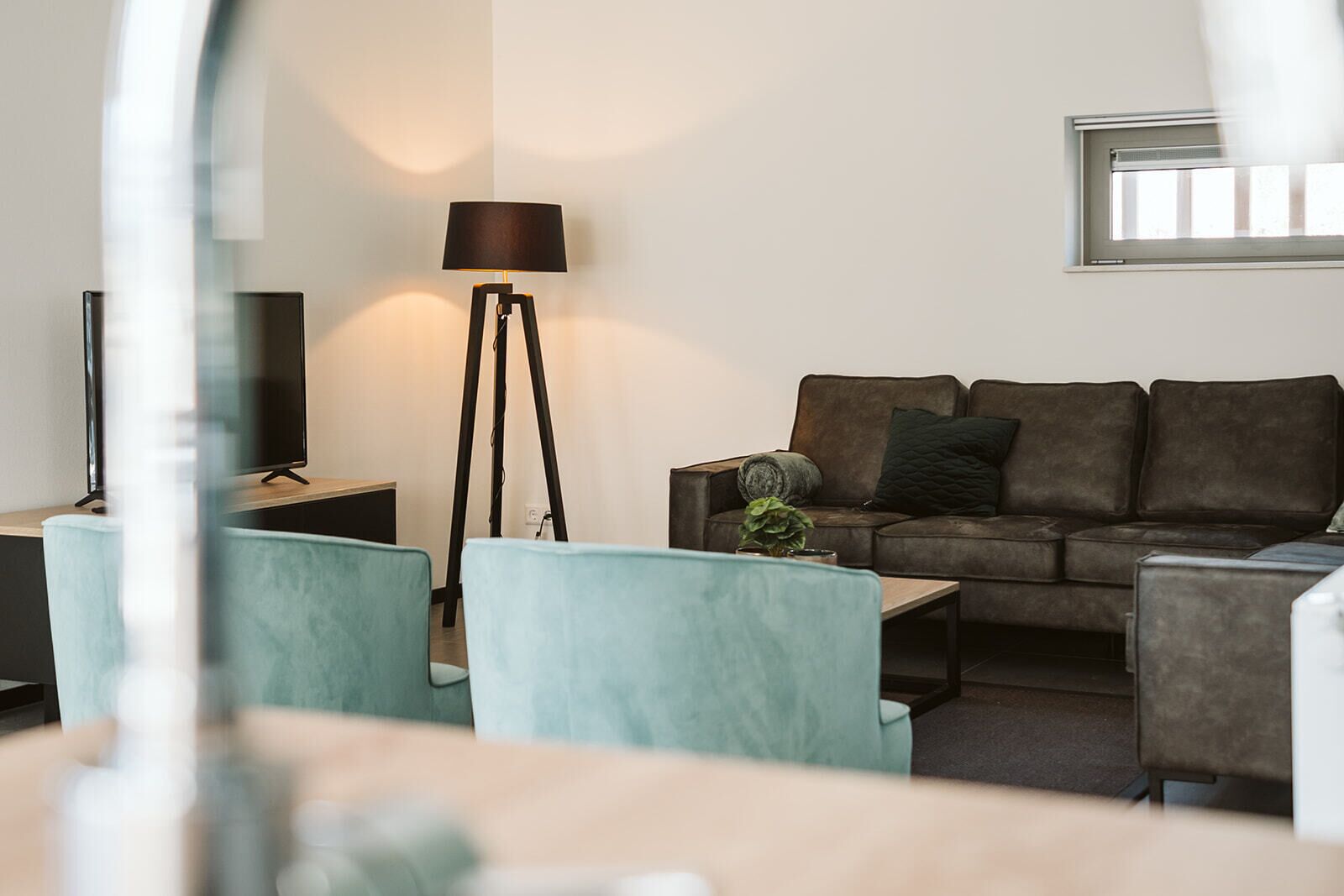 A modern living room with a sofa, two armchairs, a floor lamp, and a television.