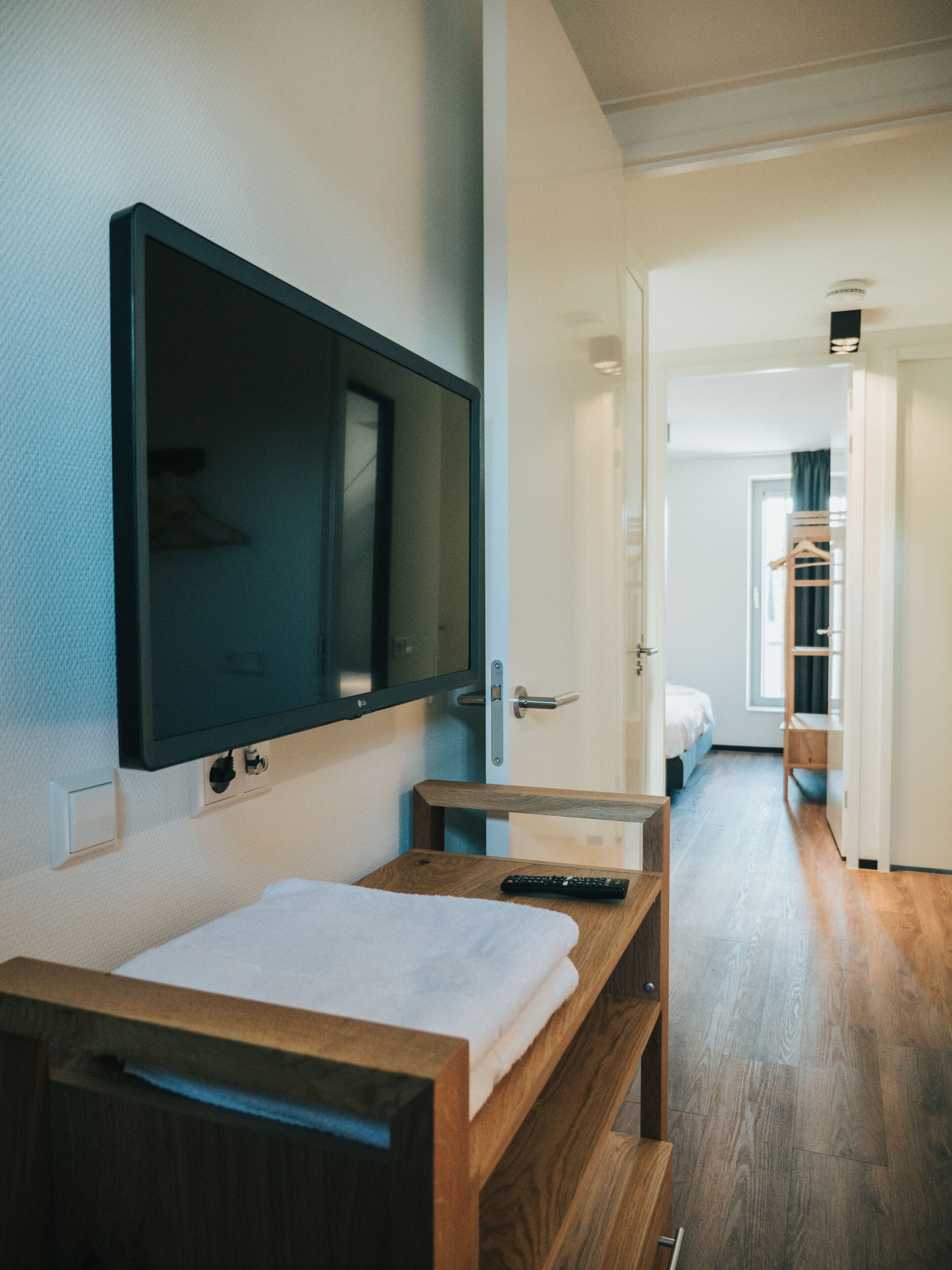 Ein modernes Hotelzimmer mit einem Holzbett, einem flachbildfernseher an der Wand und einem Flur, der zu einem Badezimmer mit einer hölzernen Sitzbank führt.