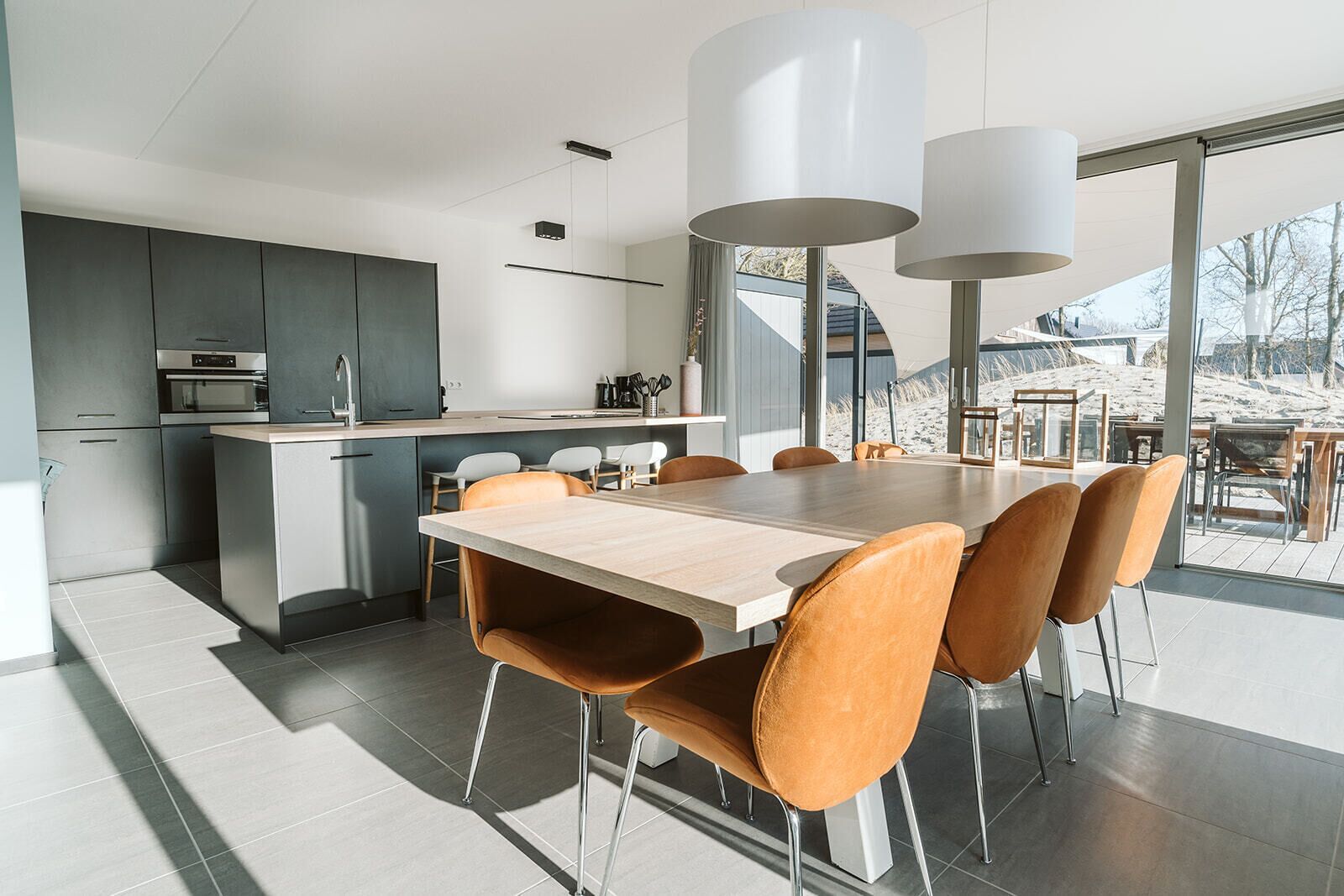 A modern kitchen with grey cabinets, a wooden dining table, and orange chairs.