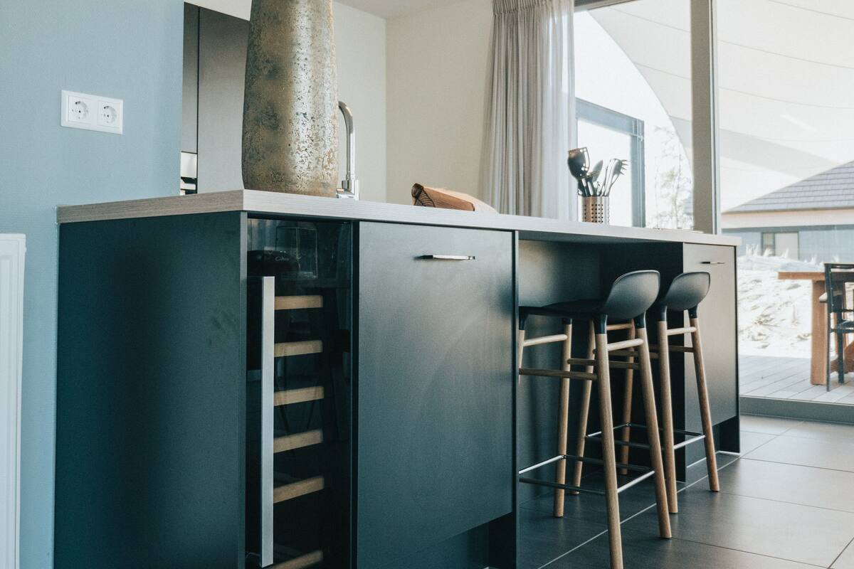 A modern kitchen with a built-in island, bar stools, and a large window offering a view of the outdoors.