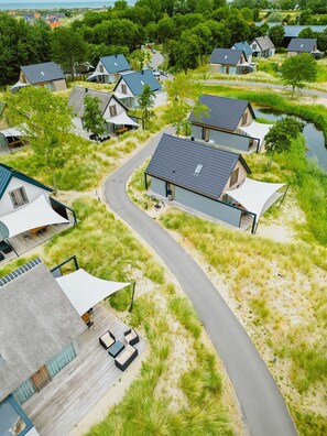 A modern residential area with houses featuring flat roofs and white walls, surrounded by grassy fields and a curved road.