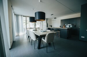Uma cozinha moderna com armários escuros, uma ilha central e uma área de refeições com uma mesa grande e cadeiras.