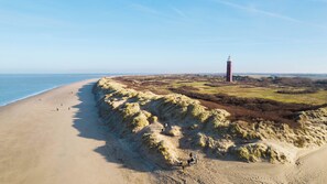 A coastal landscape with a sandy beach, dunes, and a lighthouse.