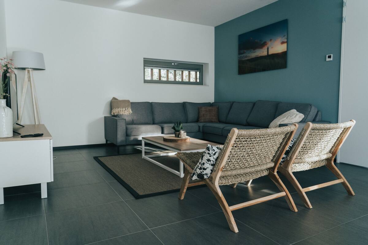 A modern living room with a grey sofa, two wicker chairs, a coffee table, and a painting on the wall.
