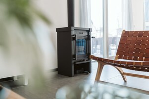 A modern living room with a black wood-burning stove, a wooden chair, and large windows.