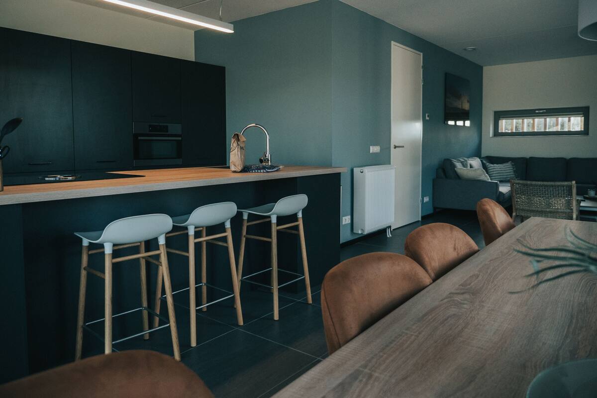 A modern kitchen with a central island, bar stools, and a dining area with a wooden table and chairs.