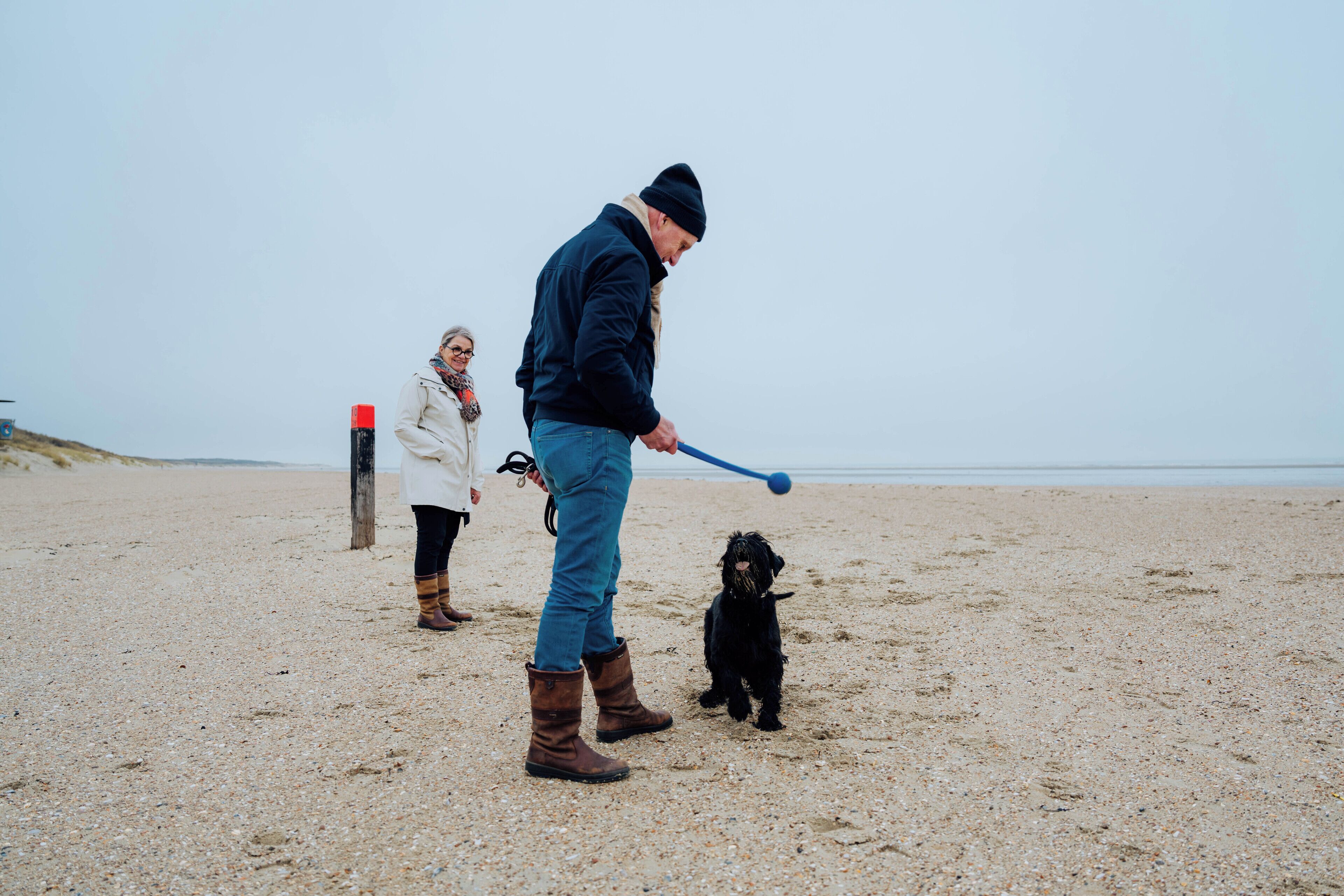 Une personne qui joue avec un chien sur une plage de sable.