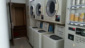 A laundry area with multiple washing machines and a shelf with detergent bottles. - OTA Daiichi Hotel (Ota)