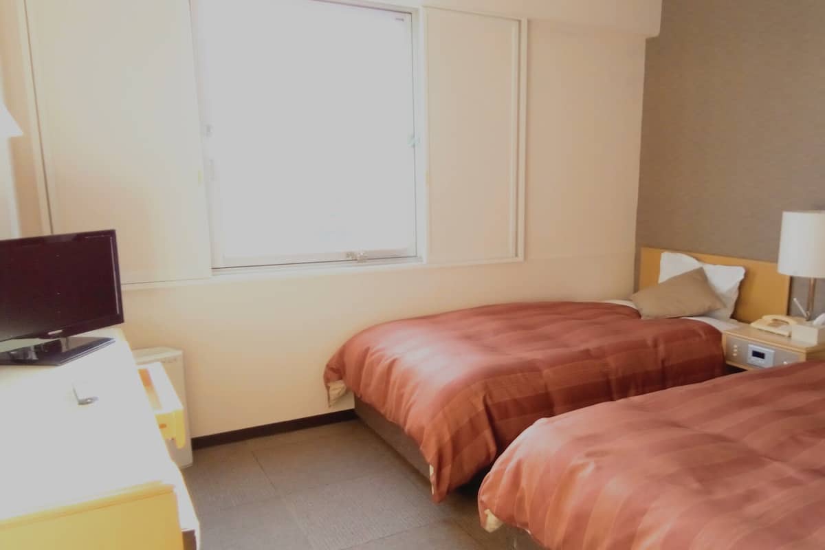 Une chambre d’hôtel avec deux lits, une télévision, une table de chevet avec une lampe et une fenêtre.