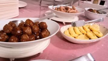 A buffet table with various dishes including glazed meatballs, sliced bananas, and other food items.