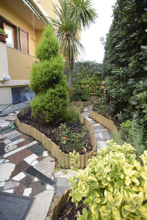 A garden with a variety of plants, a palm tree, and a stone pathway. - Casa Orata (Alghero)