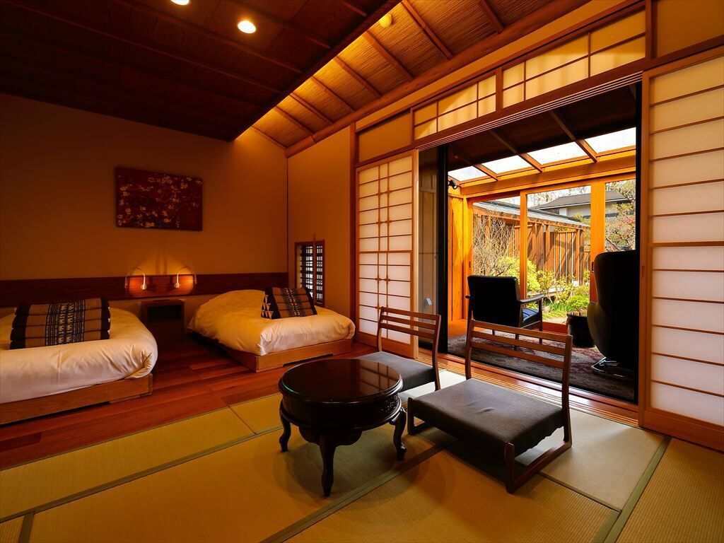 Una habitación japonesa tradicional con suelo de tatami, una mesa baja, dos futones de tatami y puertas correderas que dan a un espacio exterior.