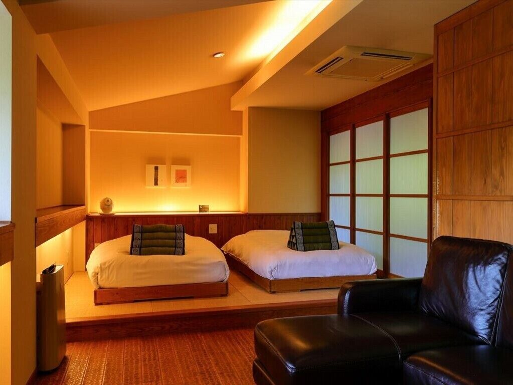 Ein Zimmer mit zwei Betten, einem schwarzen Ledersessel und einer Schiebetür mit satinierten Glasscheiben.