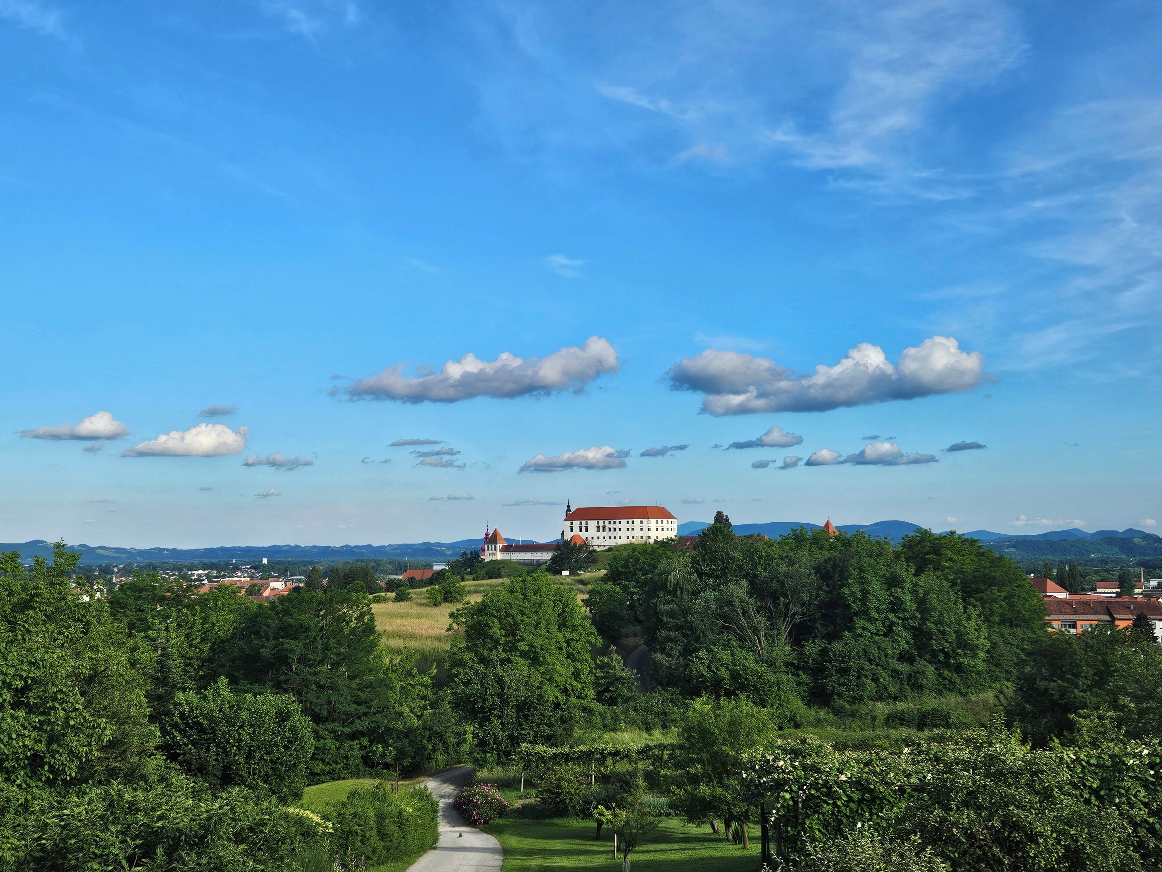 A large building with a red roof, surrounded by lush greenery and a clear blue sky.