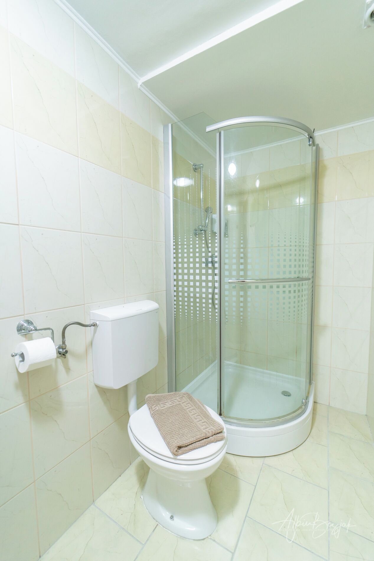 A bathroom with a toilet, a glass-enclosed shower, and a beige towel on the toilet seat.