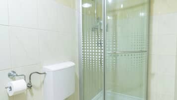 A bathroom with a toilet, a glass-enclosed shower, and a beige towel on the toilet seat.