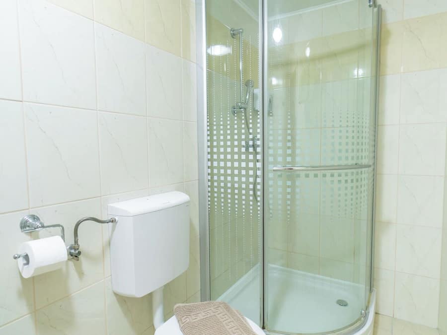 A bathroom with a toilet, a glass-enclosed shower, and a beige towel on the toilet seat.