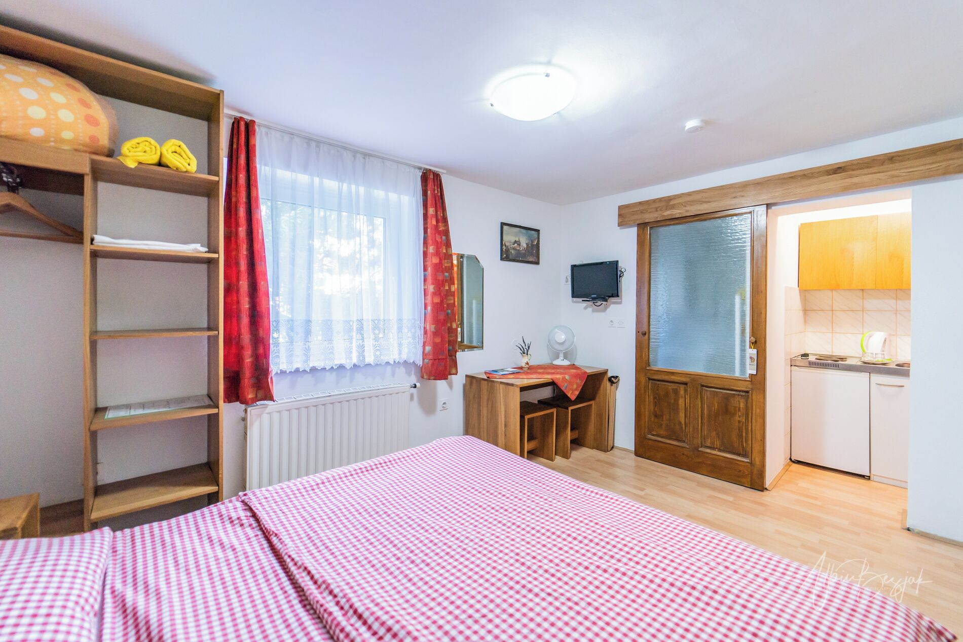 A bedroom with a bed, a desk, a radiator, a shelf with books, and a wardrobe.
