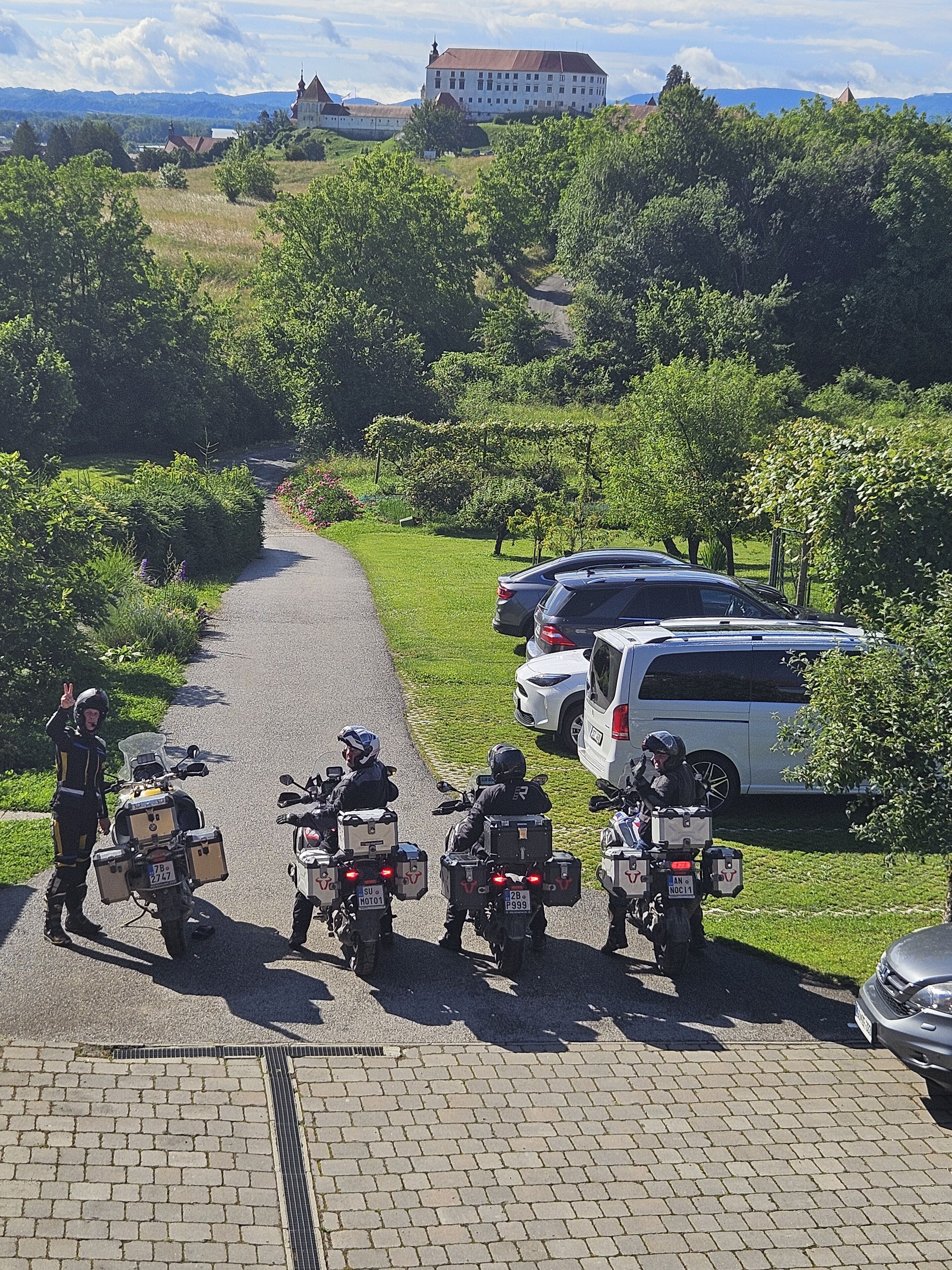 Ein gepflasterter Weg, gesäumt von parkenden Motorrädern und Autos, führt zu einem Gebäude mit rotem Dach.