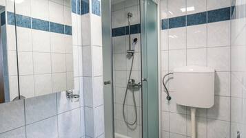 A modern bathroom with a glass-enclosed shower, a white sink, a toilet, and a bidet.