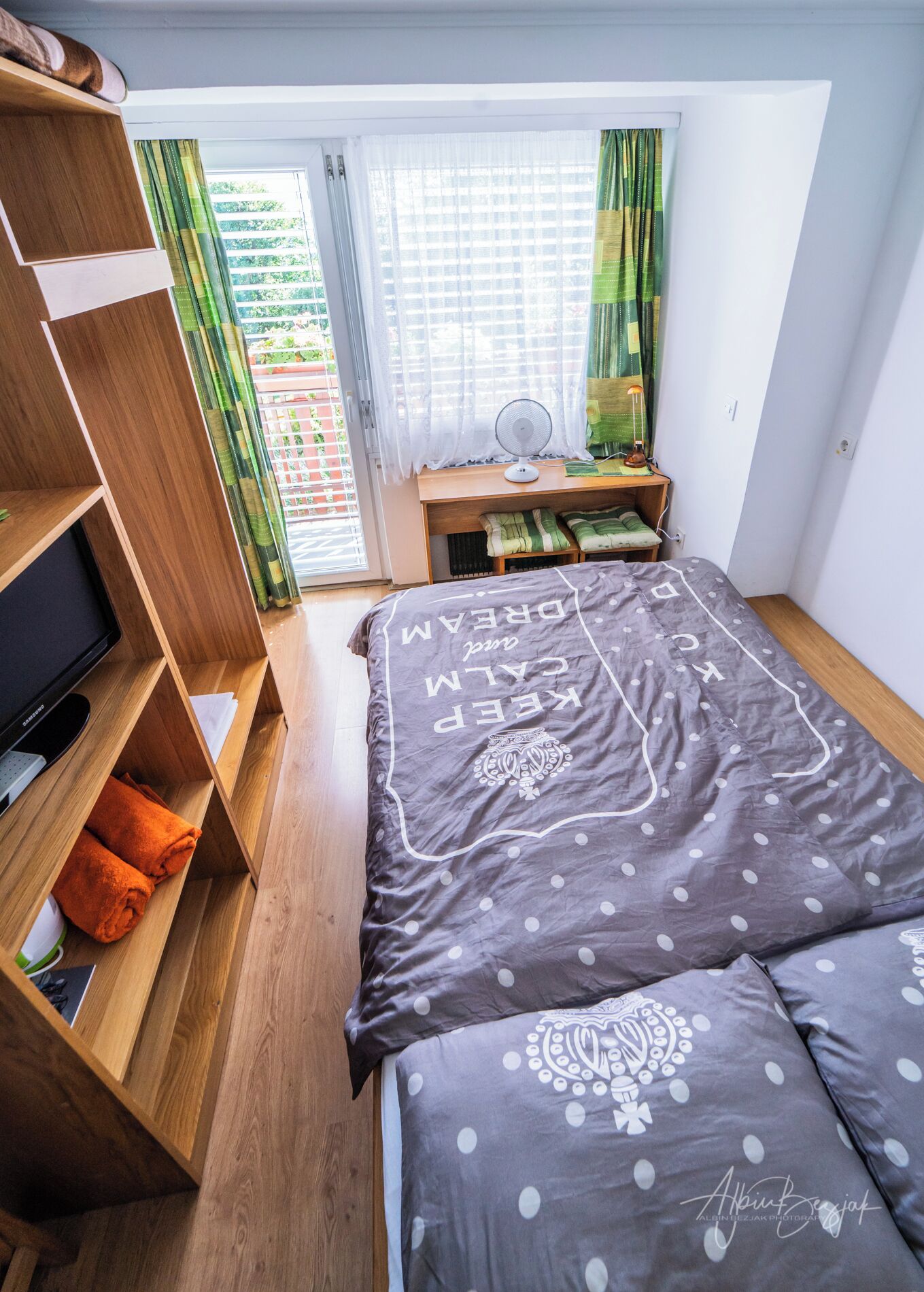Quarto com cama, estantes de madeira, escrivaninha e janela com cortinas.