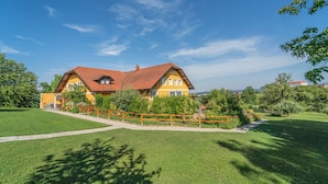 A yellow house with a red roof, surrounded by a well-maintained lawn and a wooden fence. - Panorama B&B (Ptuj)