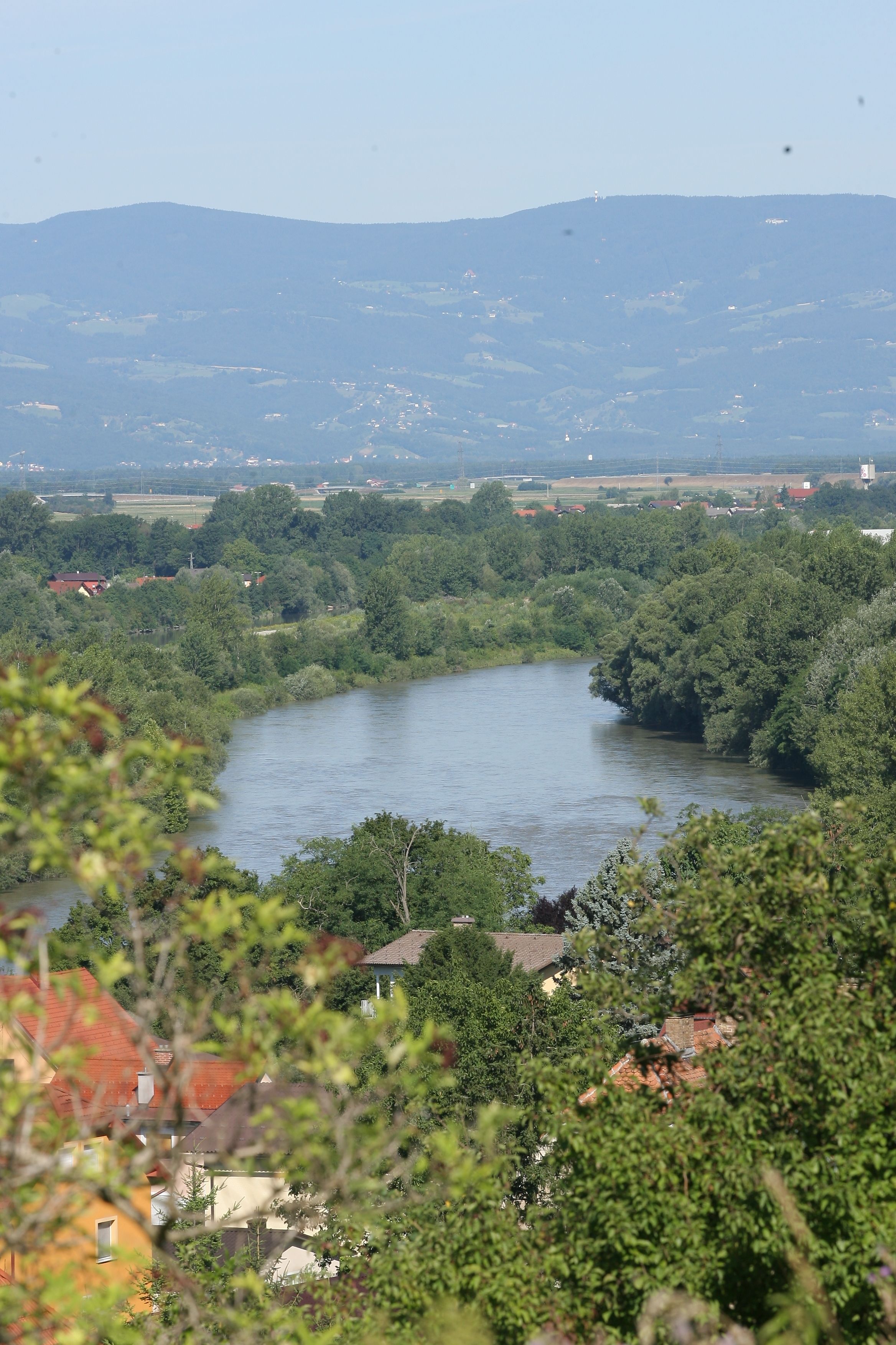 Ein Fluss, umgeben von dichter Vegetation und Häusern mit roten Dächern.