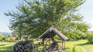 A gazebo with a metal roof and wooden beams, surrounded by a garden with various flowering plants and a large tree providing shade. - Panorama B&B (Ptuj)