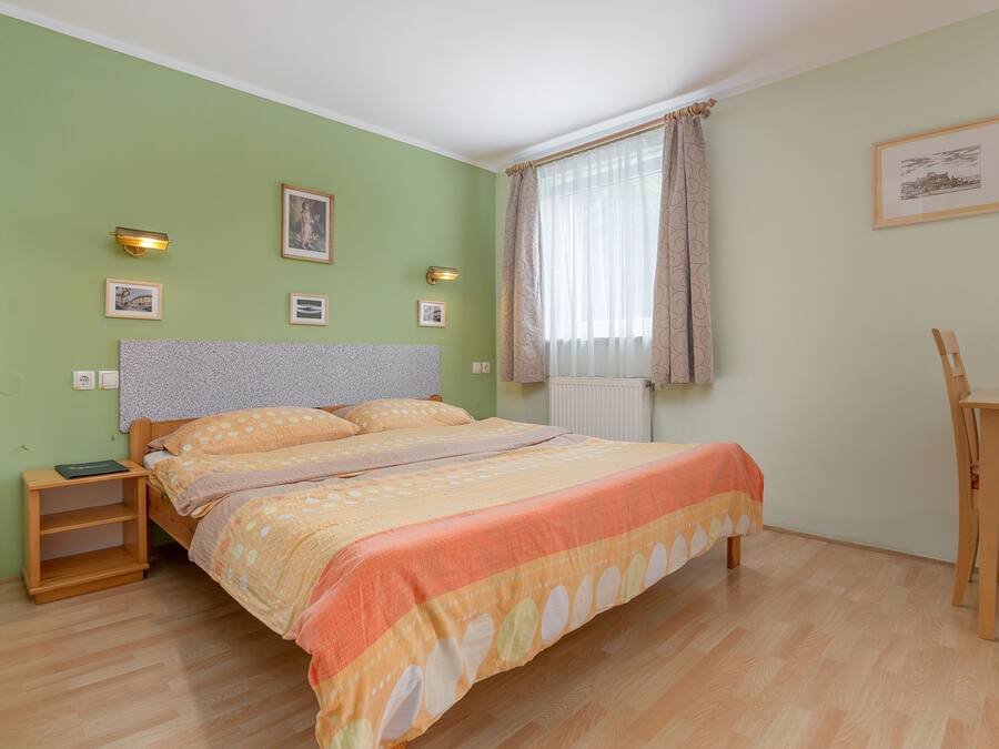 A bedroom with a bed, nightstands, a chair, and a window with curtains.
