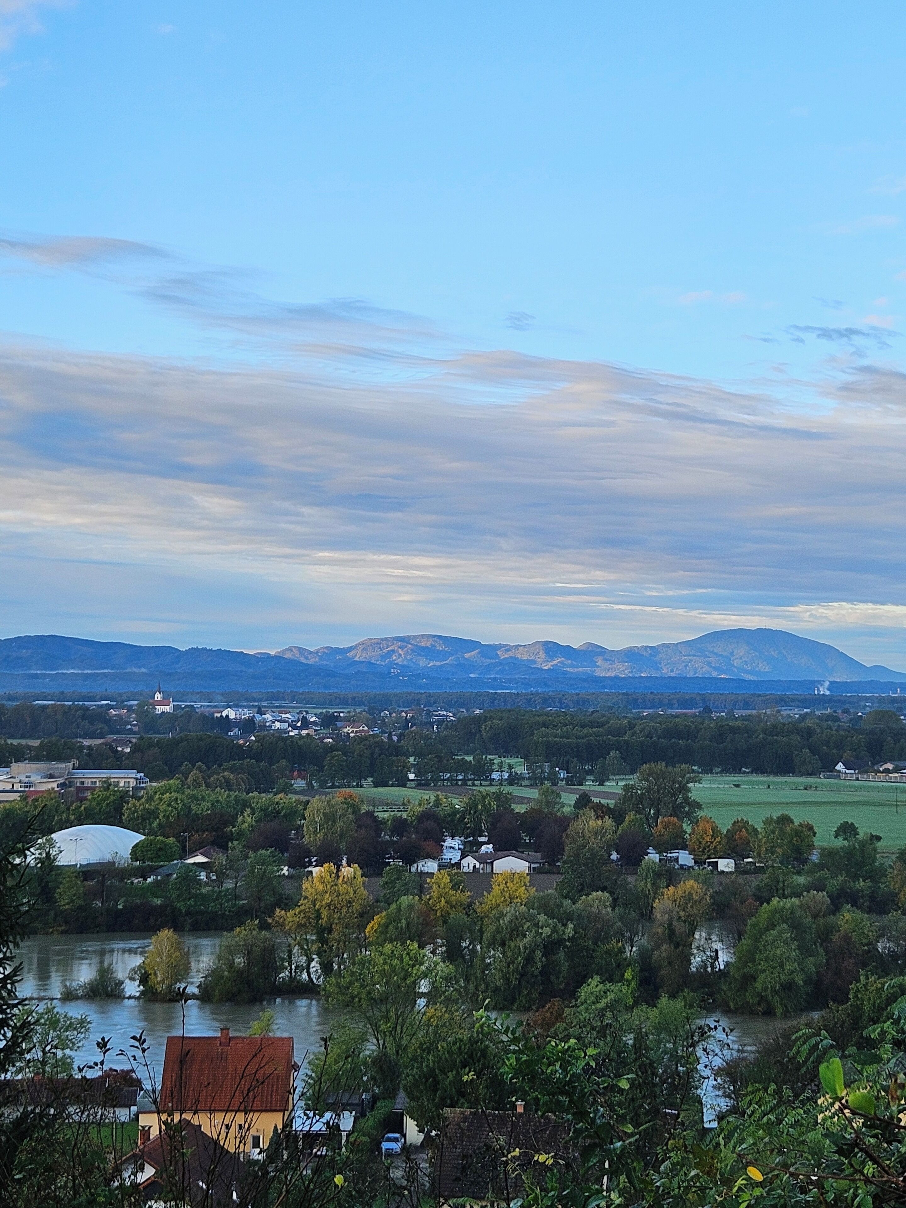 A panoramic view of a town with houses, a river, and mountains in the background.