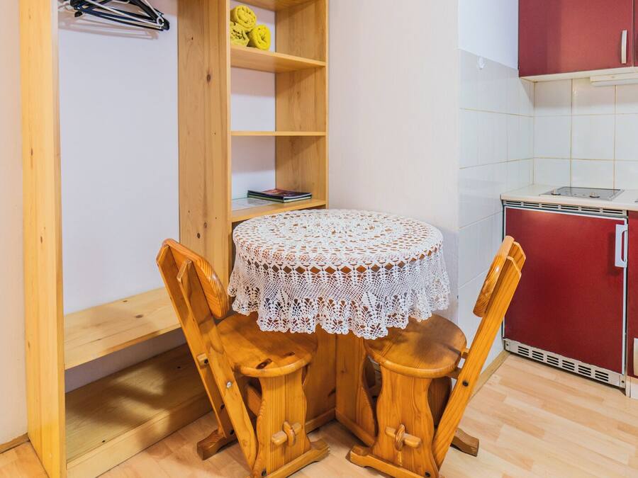 Quarto compacto com guarda-roupa de madeira, uma mesa redonda pequena com toalha de renda e um armário vermelho.