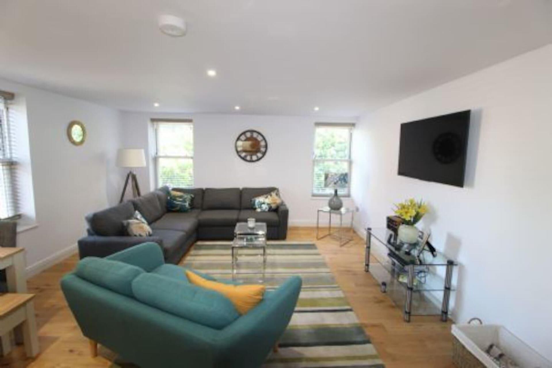 Ein Wohnzimmer mit einem Ecksofa, einem türkisfarbenen Sessel, einem Couchtisch und einem an der Wand montierten Fernseher.