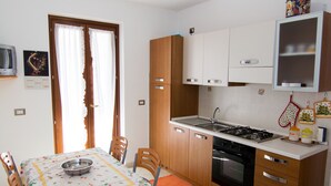 A compact kitchen with a dining table, chairs, a stove, sink, and cabinets. - Casa Grongo (Alghero)
