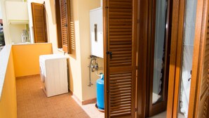 A hotel room with a washing machine, a blue gas cylinder, and wooden shutters on the door. - Casa Grongo (Alghero)