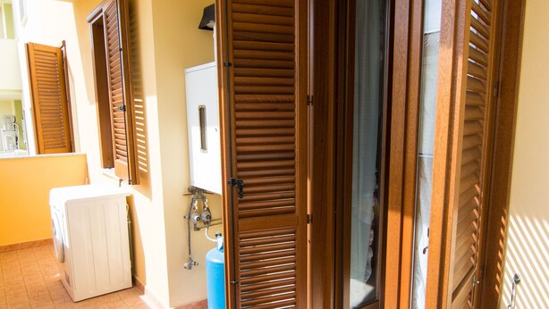 A hallway with wooden doors, a washing machine, and a blue water heater. - Casa Grongo (Alghero)