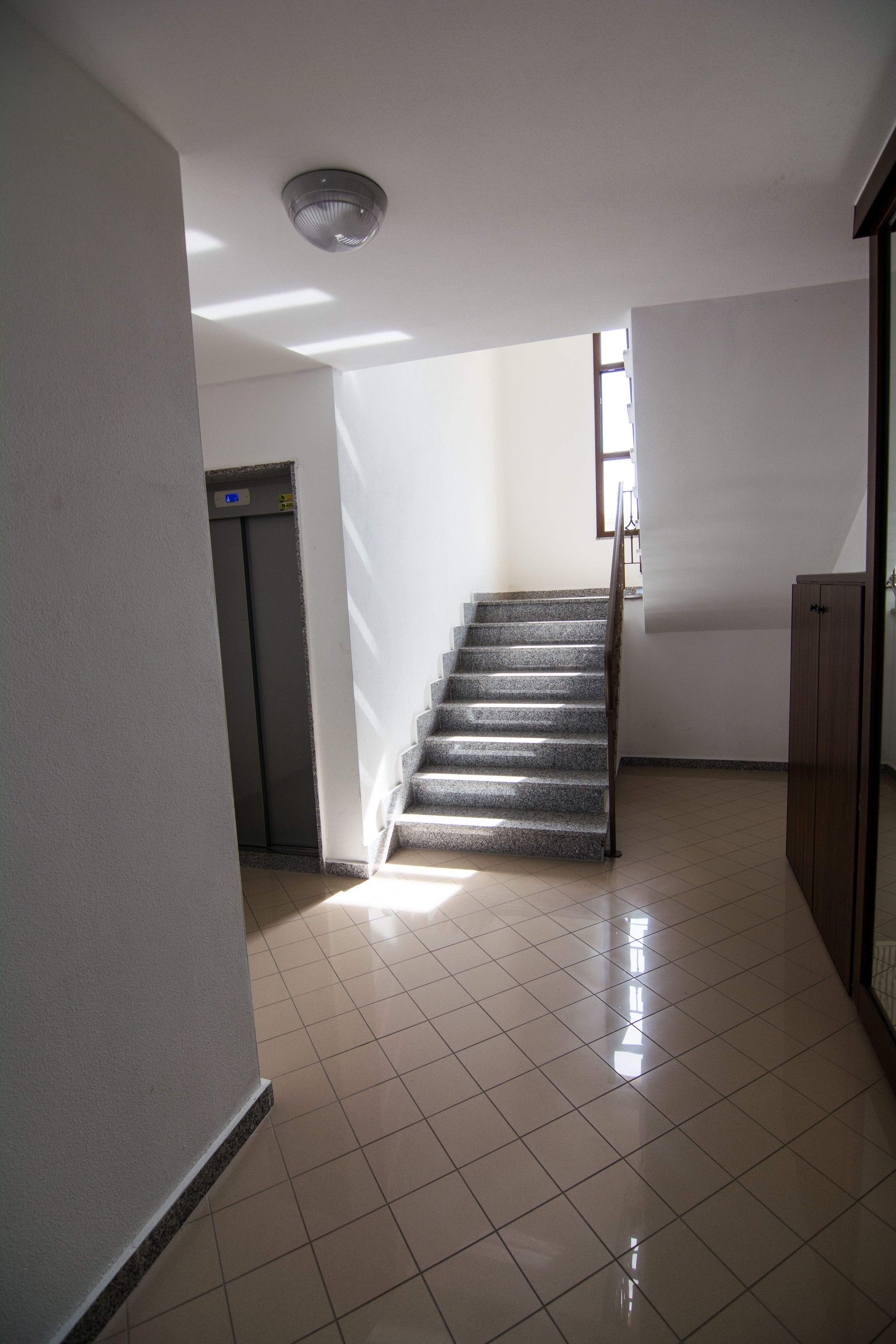 A staircase leading to an elevator in a hallway with tiled floors and plain walls.
