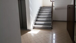 A staircase leading to an elevator in a hallway with tiled floors and plain walls. - Casa Grongo (Alghero)