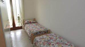 A room with two single beds, a wooden wardrobe, a mirror, and a window with sheer curtains. - Casa Murena (Alghero)