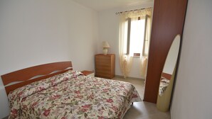 A bedroom with a bed, a dresser, a lamp, and a mirror. - Casa Murena (Alghero)