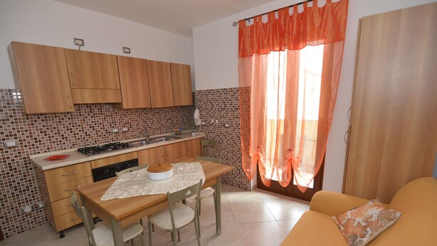 A compact kitchen with wooden cabinets, a dining table, and chairs. - Casa Murena (Alghero)