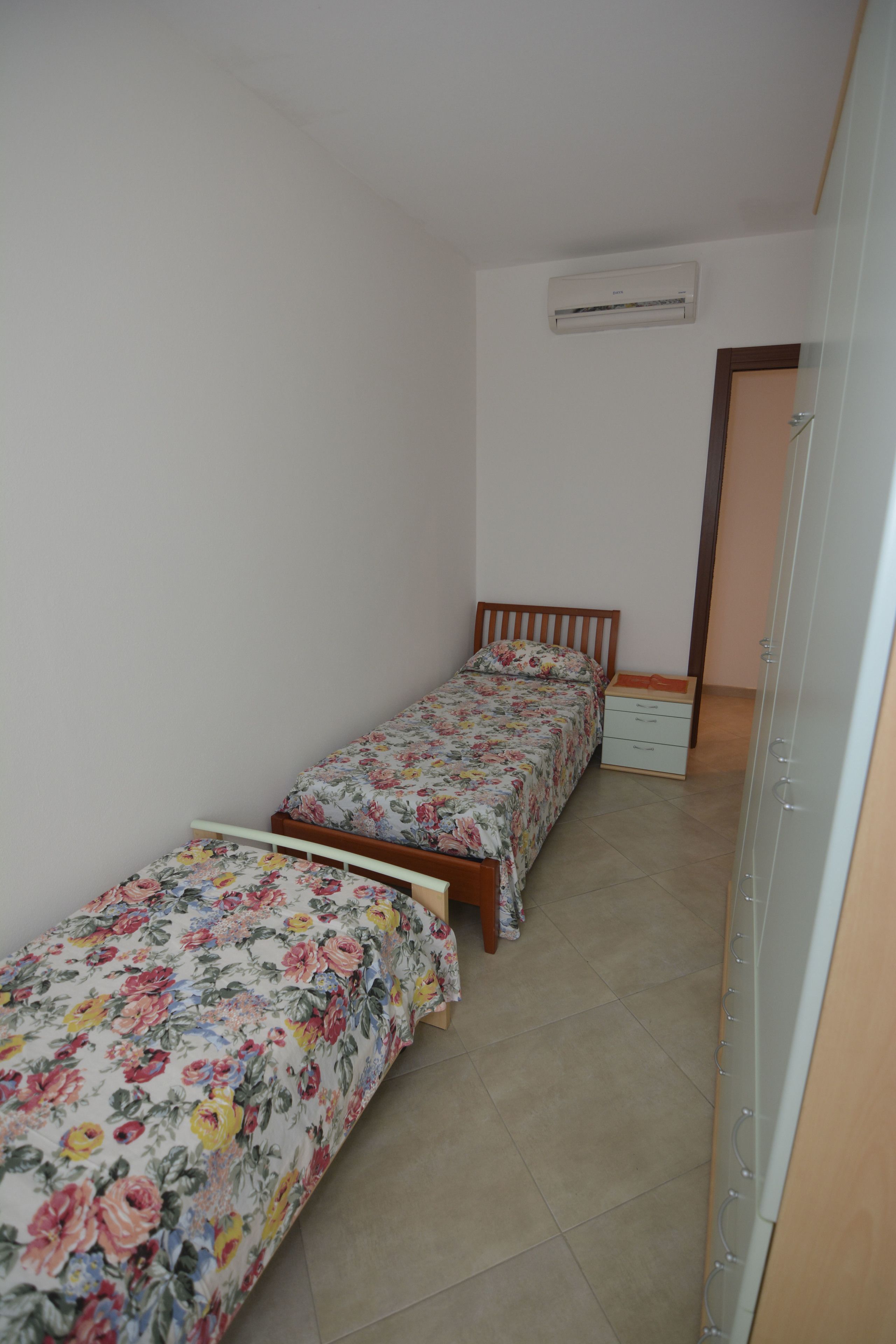 A bedroom with two single beds, a wardrobe, and an air conditioning unit on the wall.