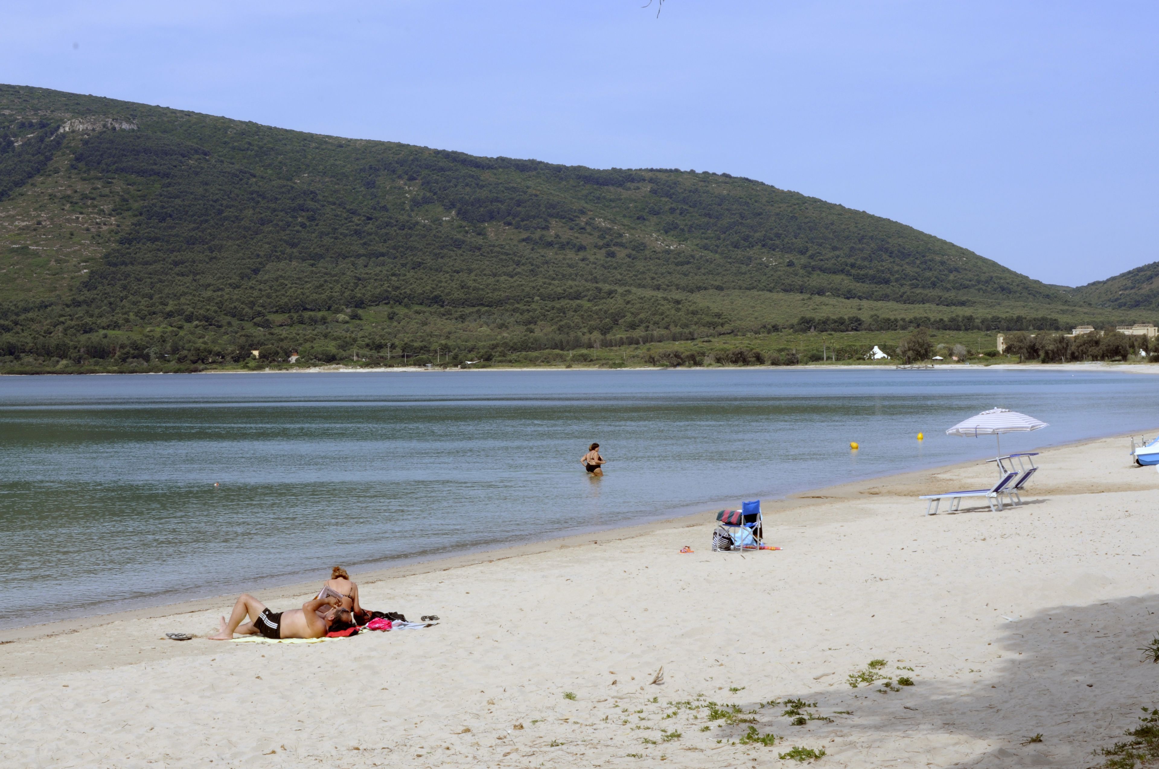 A beach with a clear view of the water and a hilly landscape in the background.