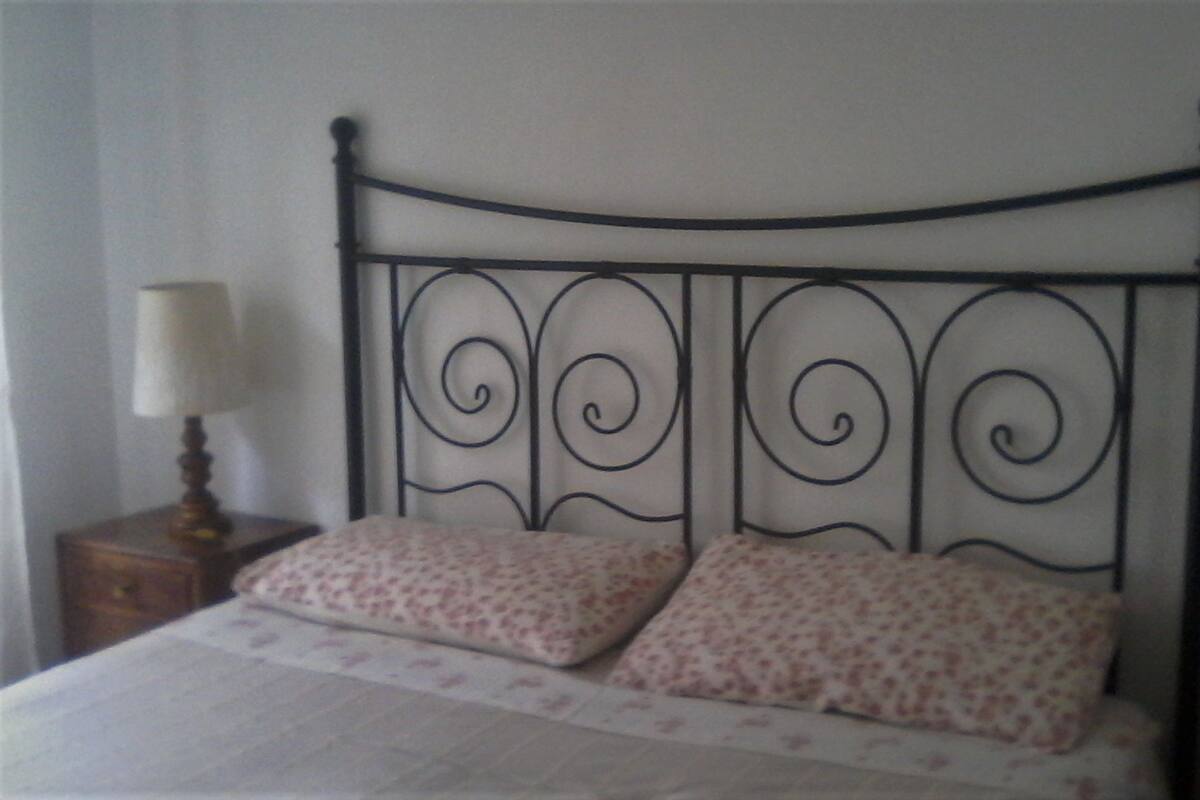A bed with a metal headboard, two pillows, and a bedside table with a lamp.
