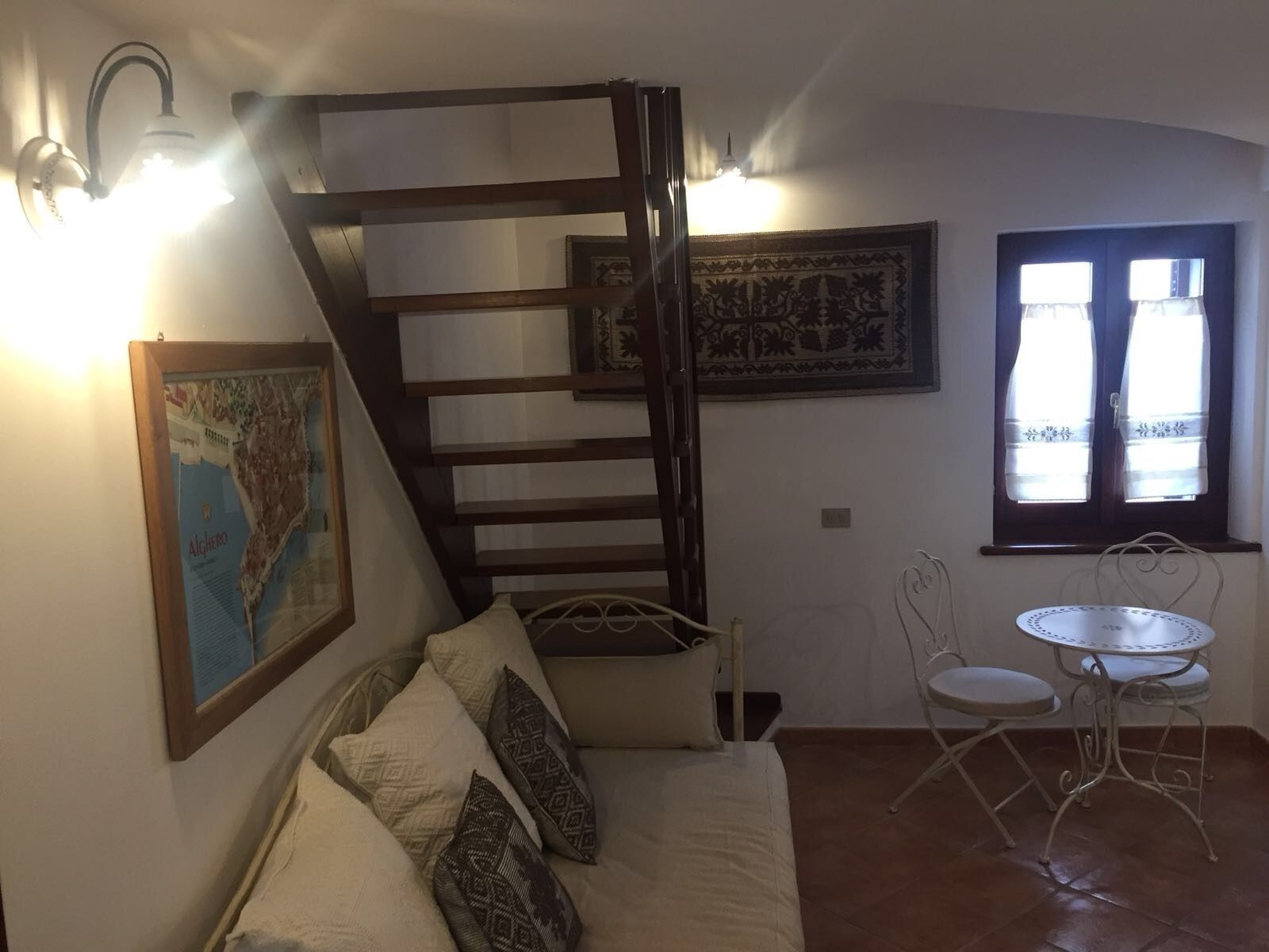 A cozy room with a bed, a small table, a chair, a staircase, and a window with curtains.