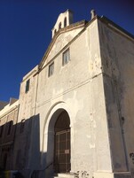 Un edificio histórico con una amplia entrada en arco, una torre de campanas y una fachada desgastada por el tiempo.