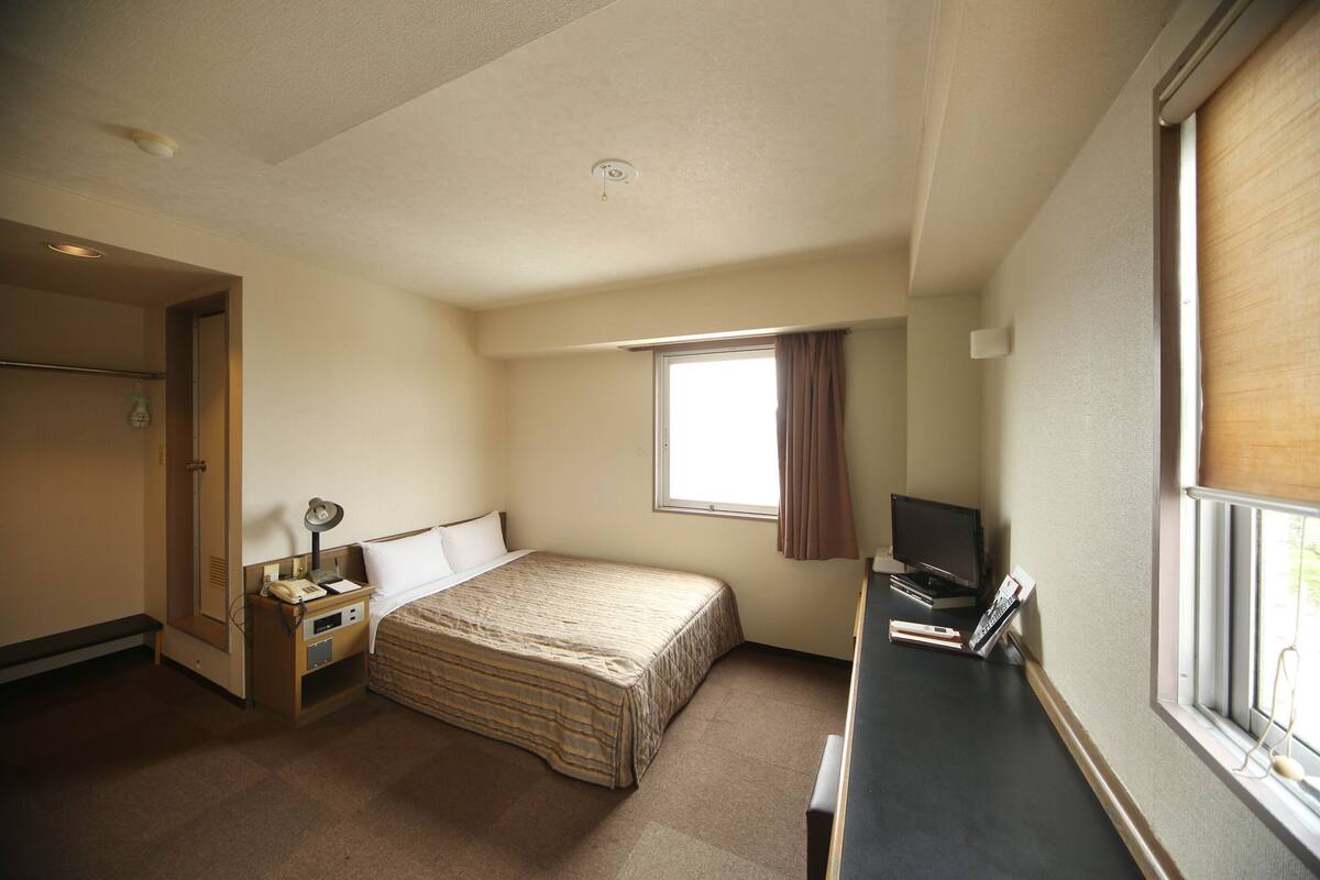 A hotel room with a bed, a desk, a chair, a window with curtains, and a television.