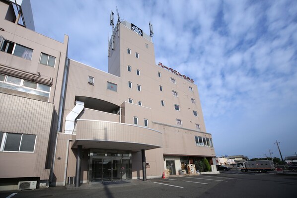 A multi-story hotel with a modern design, featuring a prominent entrance with a covered walkway and a parking area in front. - Harvest Hotel (Isesaki)