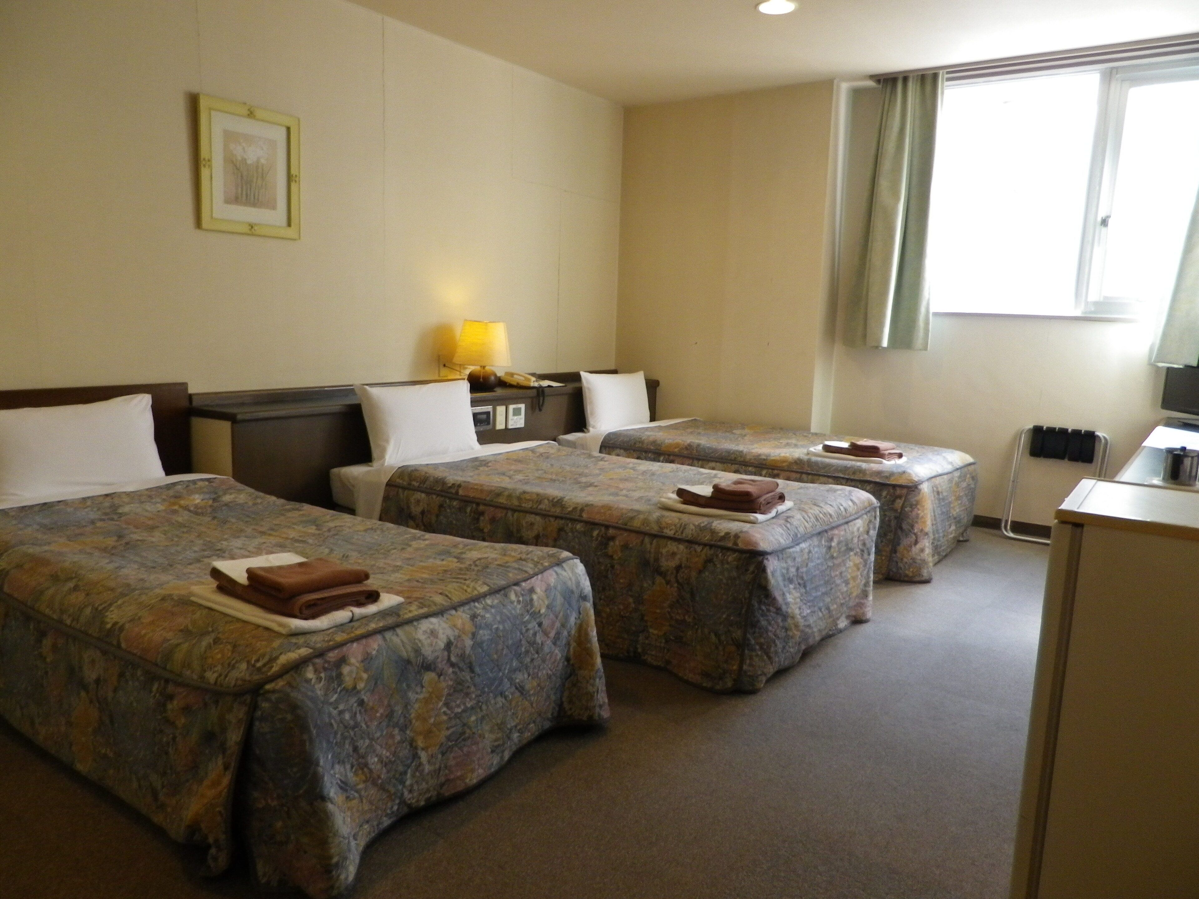 Habitación de hotel con dos camas, un escritorio, una lámpara y una ventana con cortinas.